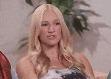 a blonde woman is making a funny face while sitting on a couch in front of a plant .