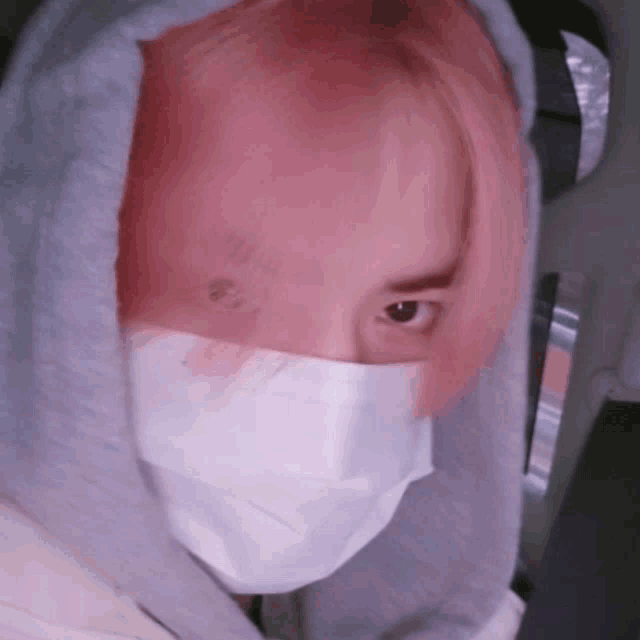a person with pink hair wearing a face mask and a hoodie