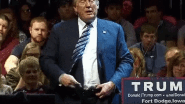a man in a suit and tie stands in front of a sign that says " trum "