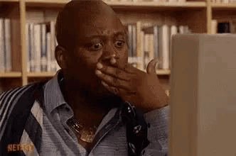 a man is covering his mouth with his hand while looking at a computer screen .