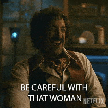 a man with curly hair and a scarf around his neck says " be careful with that woman "