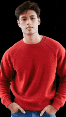 a man wearing a red sweater and blue jeans stands with his hands in his pockets