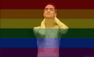 a man is standing in front of a rainbow flag and covering his face with his hands .