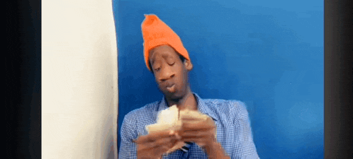 a man wearing an orange hat and a blue plaid shirt is eating a sandwich .