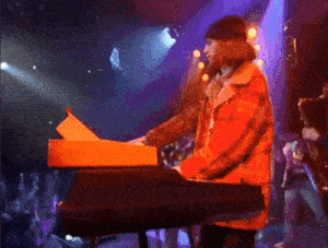 a man in a red plaid jacket is playing an orange keyboard on a stage
