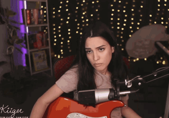 a woman playing a guitar in front of a microphone with the name kiger on the bottom right