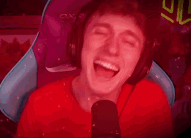a man wearing headphones is laughing in front of a microphone while sitting in a gaming chair .