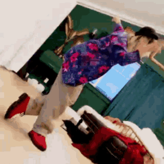 a person in a floral shirt and red shoes is dancing in a room with a bed .