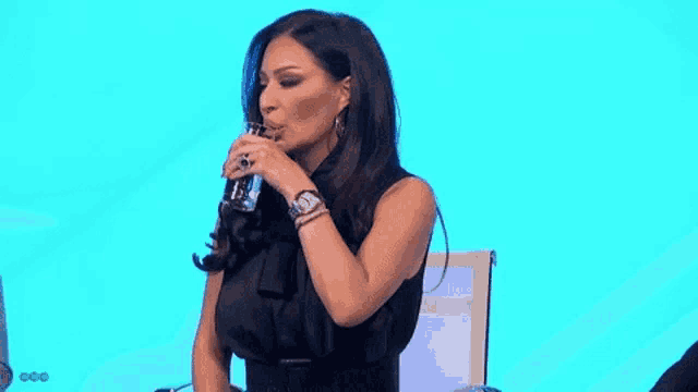 a woman in a black dress is sitting in a chair holding a glass of water .