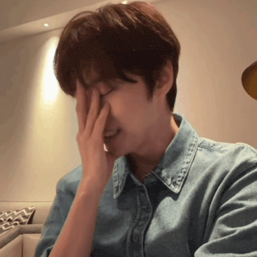 a man wearing a denim shirt covering his face with his hand