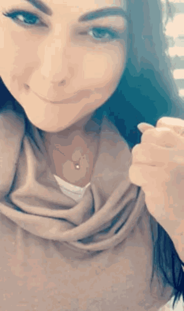 a woman wearing a scarf and a necklace smiles at the camera