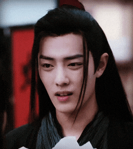 a young man with long black hair is holding a piece of paper in his hand