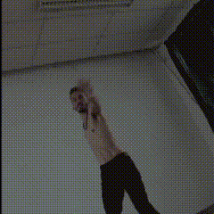a man with a beard is standing in front of a window wearing a black tank top and a necklace .
