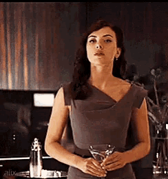 a woman in a grey dress is holding a martini glass in her hands .