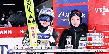a couple of skiers standing next to each other with one holding a sign that says yuki ito