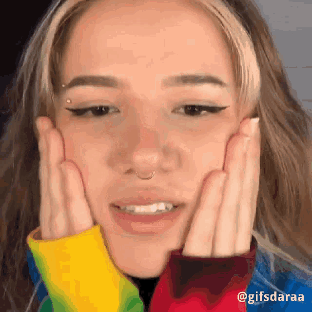 a woman with her hands on her face is wearing a rainbow sweater