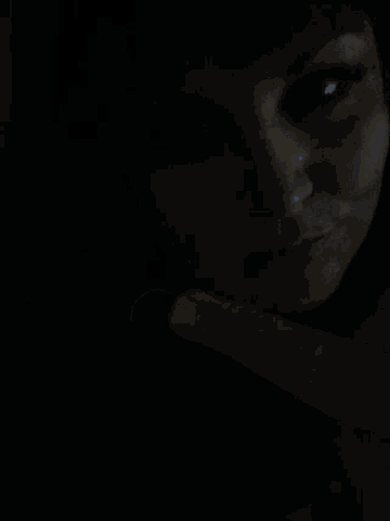 a close up of a woman 's face in the dark with her finger on her face .