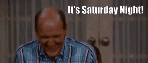 a bald man is sitting at a table laughing with the words `` it 's saturday night '' written above him .