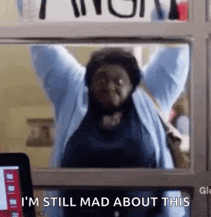 a woman is standing in front of a window with her arms in the air and says `` i 'm still mad about this ''