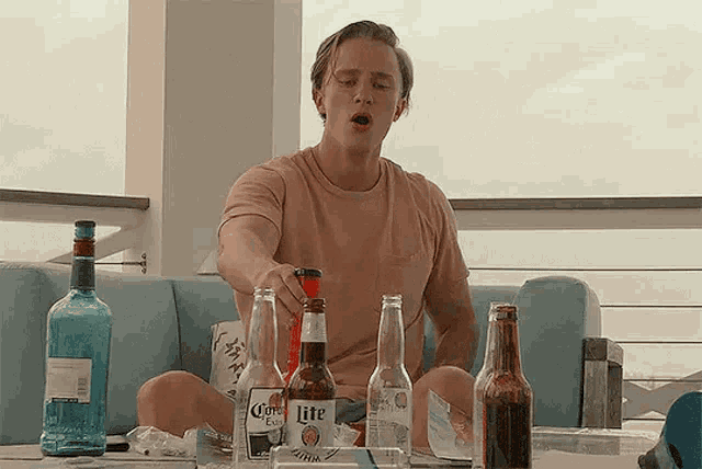 a man is sitting on a couch holding a bottle of lite beer