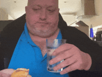 a man in a blue shirt is holding a glass of water and a piece of food