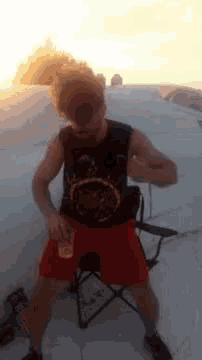 a man in a black tank top and red shorts is holding a drink