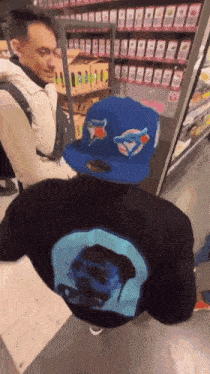 a man wearing a blue jays hat is standing next to another man wearing a black sweatshirt .