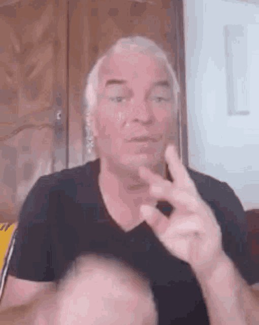 a man with gray hair and a black shirt is making a peace sign with his finger .