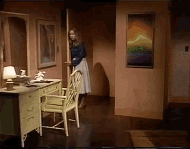 a woman standing in a room with a painting on the wall behind her