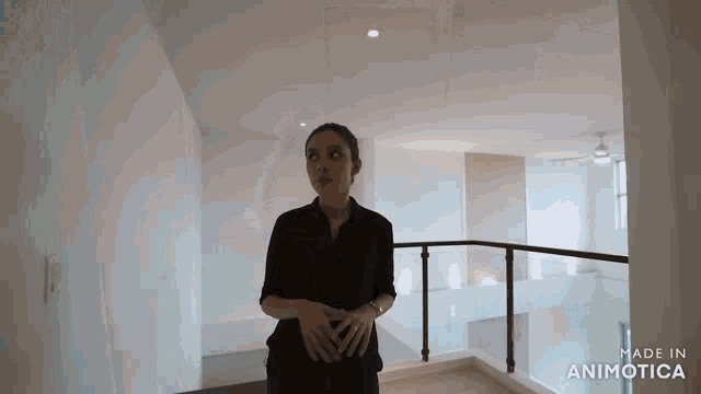 a woman in a black shirt is standing on a balcony in an empty room with a ceiling fan .