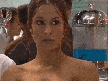 a woman without a shirt is standing in front of a blue dispenser .