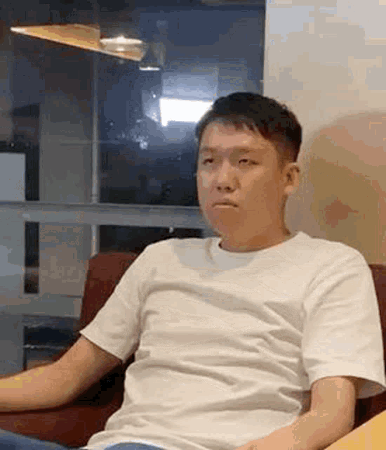a man in a white t-shirt is sitting on a red couch and making a funny face .