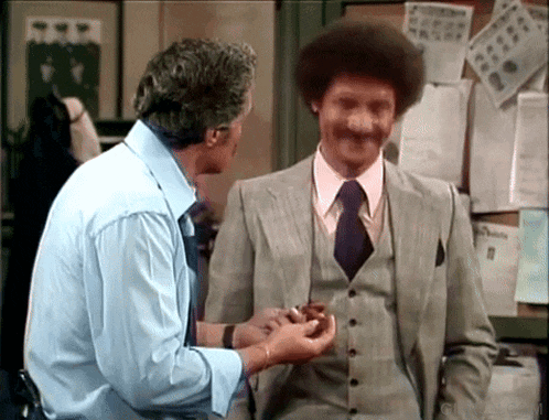 a man in a suit and tie talks to another man in a blue shirt