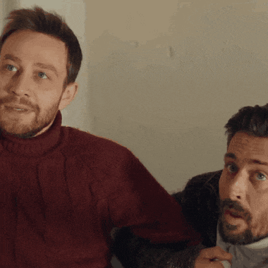 a man with a beard wearing a red sweater is sitting next to another man