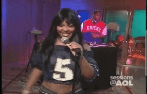a woman is singing into a microphone while wearing a number 5 shirt