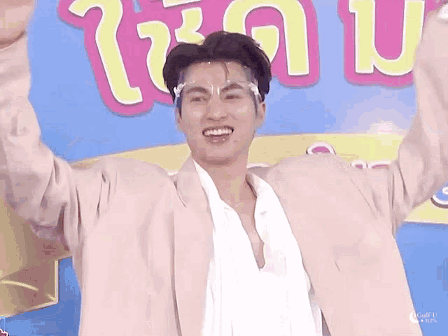 a man wearing a white shirt and a pink jacket is standing with his arms in the air .