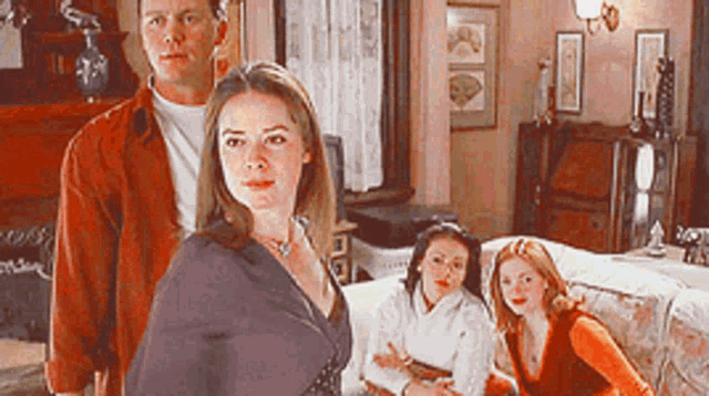a man and three women are standing in a room with a bed