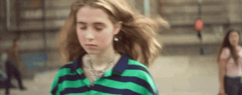 a girl in a green and blue striped shirt is walking down a street .