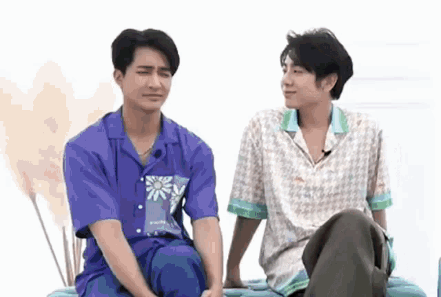 two young men are sitting next to each other on a couch . one of the men is wearing a purple shirt .