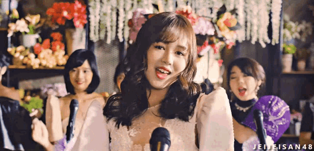 a woman in a white dress stands in front of a microphone with the hashtag jeiteisan48 on the bottom