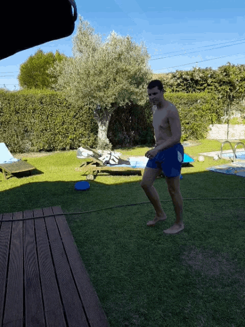 a shirtless man in blue shorts is standing on a lush green lawn