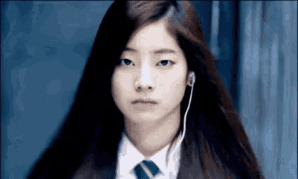 a girl in a school uniform and tie is wearing headphones and looking at the camera .