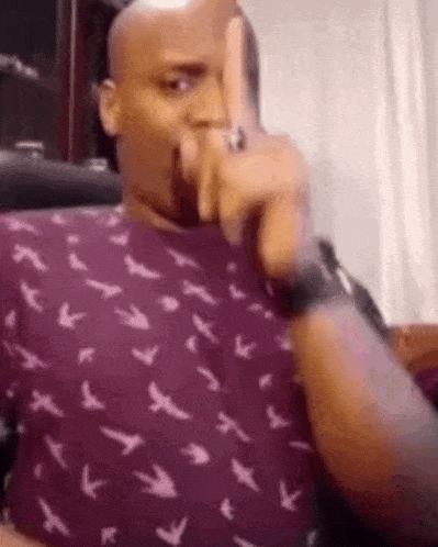 a man in a purple shirt is sitting in a chair making a funny face .