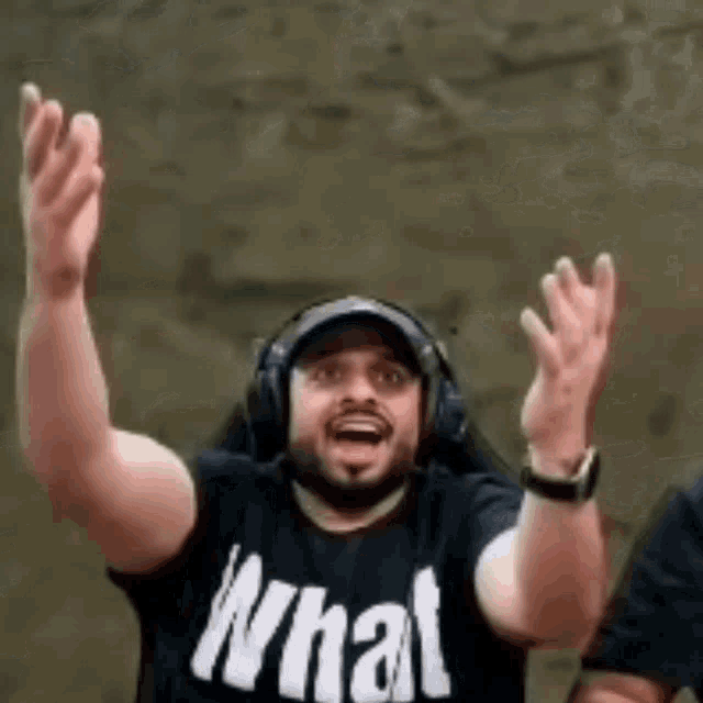 a man wearing headphones and a t-shirt that says `` what '' is raising his hands in the air .