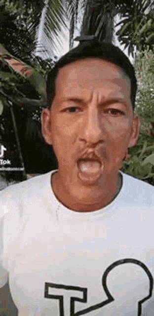 a man is making a funny face while wearing a white shirt .