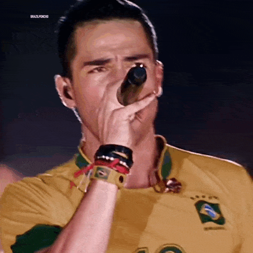 a man is singing into a microphone while wearing a yellow shirt with the brazilian flag on it .