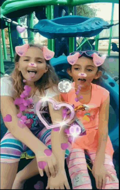 two little girls wearing pig nose masks are sitting next to each other at a playground