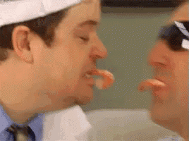 two men are eating shrimp together and one of them is holding a shrimp in his mouth .