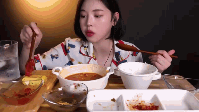 a woman is sitting at a table with bowls of food and a spoon in her hand