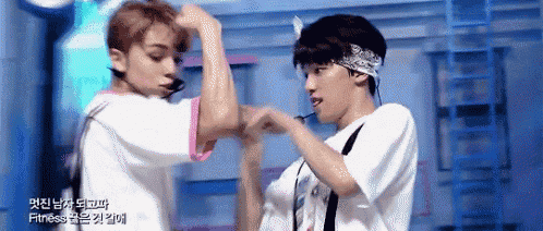two young men are flexing their muscles on a stage and one of them is wearing a bandana on his head .
